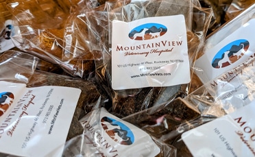 A close-up of several clear plastic bags labeled “MountainView Veterinary Hospital,” each containing dark brown pet treats. The label includes the hospital’s contact information and a mountain logo.